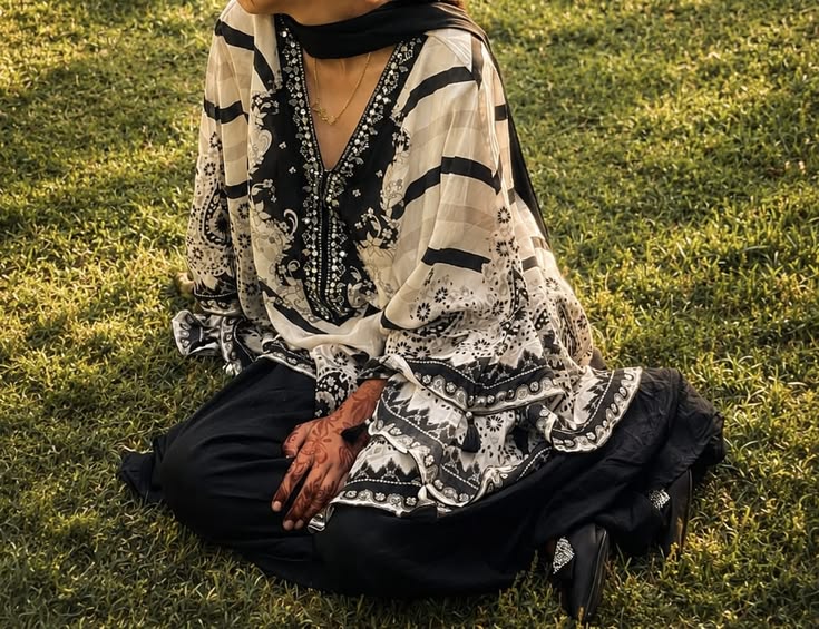 Indian woman seated on grass at golden hour in a black-and-white printed kurta with a black dupatta and palazzo, mehendi on her hands, a relaxed ethnic essential look