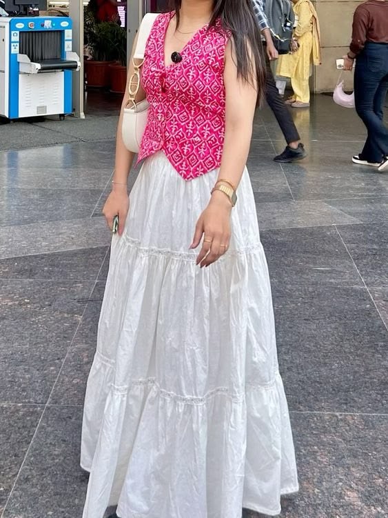 Indian woman styling a fusion ethnic essential look: a pink bandhani-print tie-up top with a white tiered maxi skirt, crossbody bag, and minimal jewellery